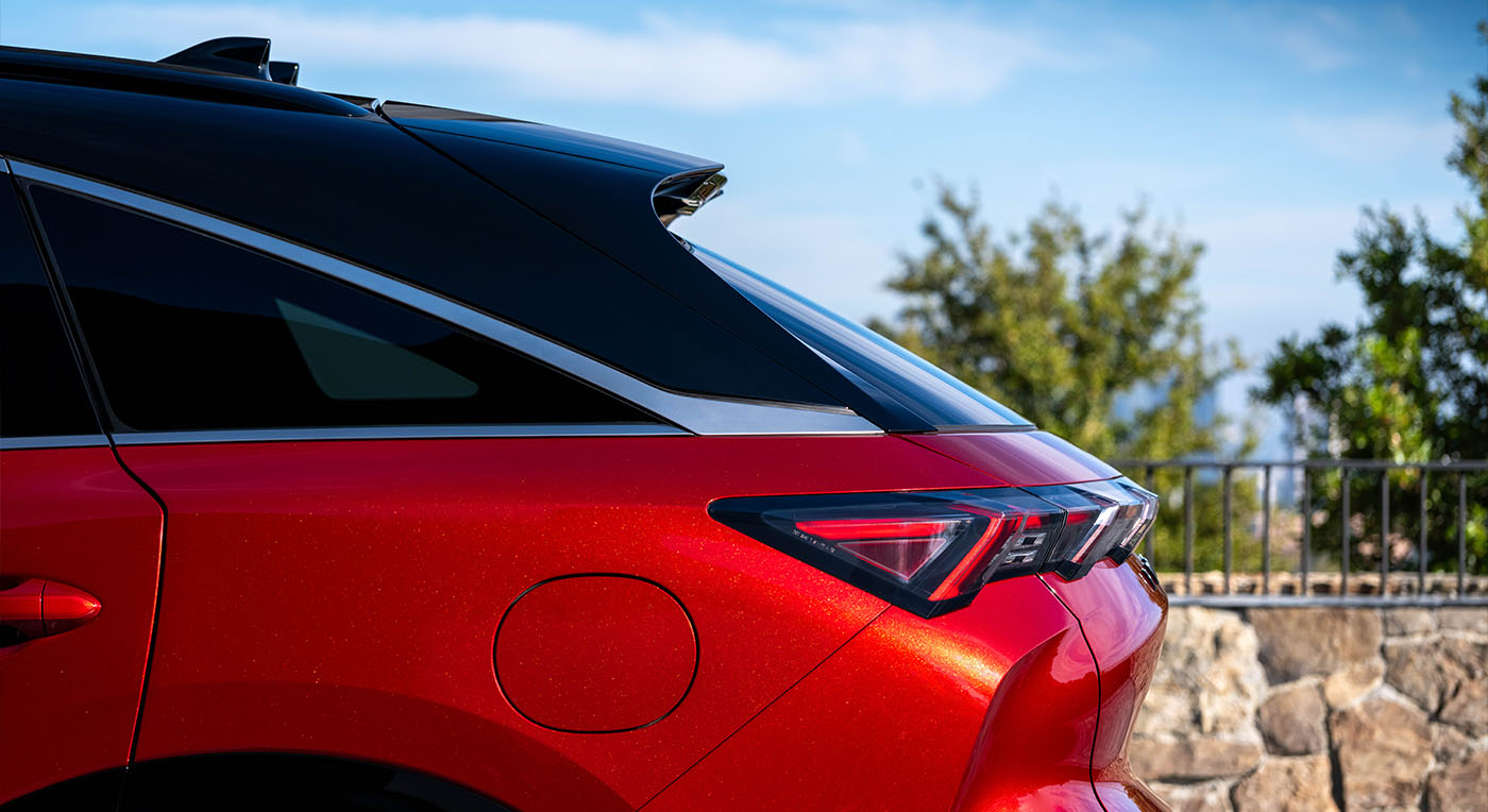 Sleek red Infiniti QX65 car with tinted windows and modern rear light design, parked near a stone wall. Background features trees and a clear blue sky.